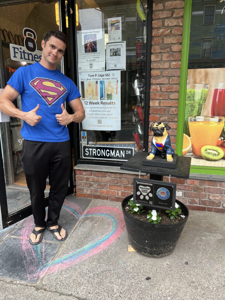 Eric Moss wearing a Superman t-shirt posing with the pug of steel outside his personal training studio on Main Street in Boonton